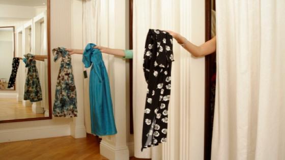 Three women behind curtains in changing room, holding out dresses